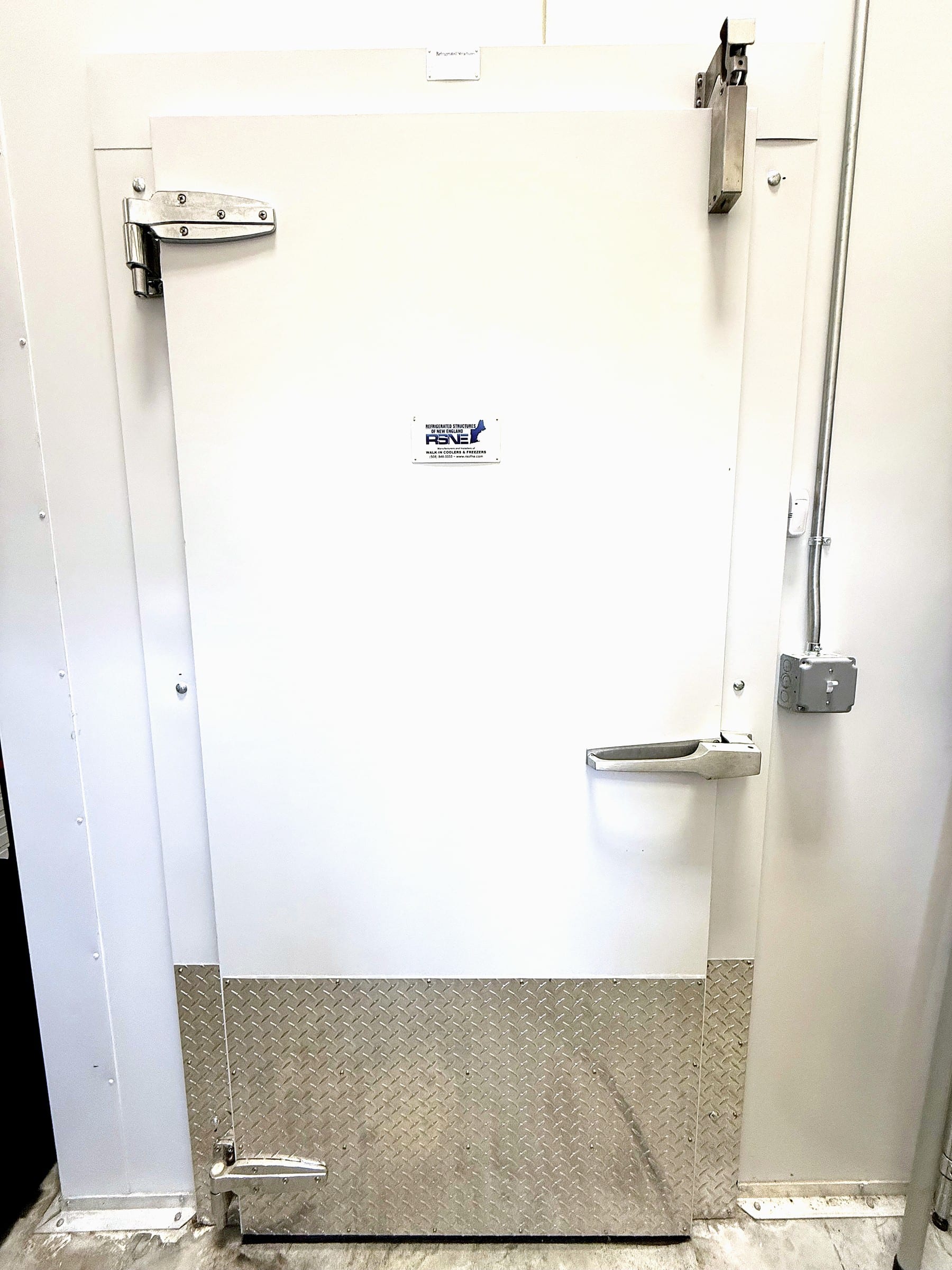 RSNE insulated swing door at Black Hat Brew Works in Bridgewater, MA, with a diamond-plate kick panel and a nameplate at eye height