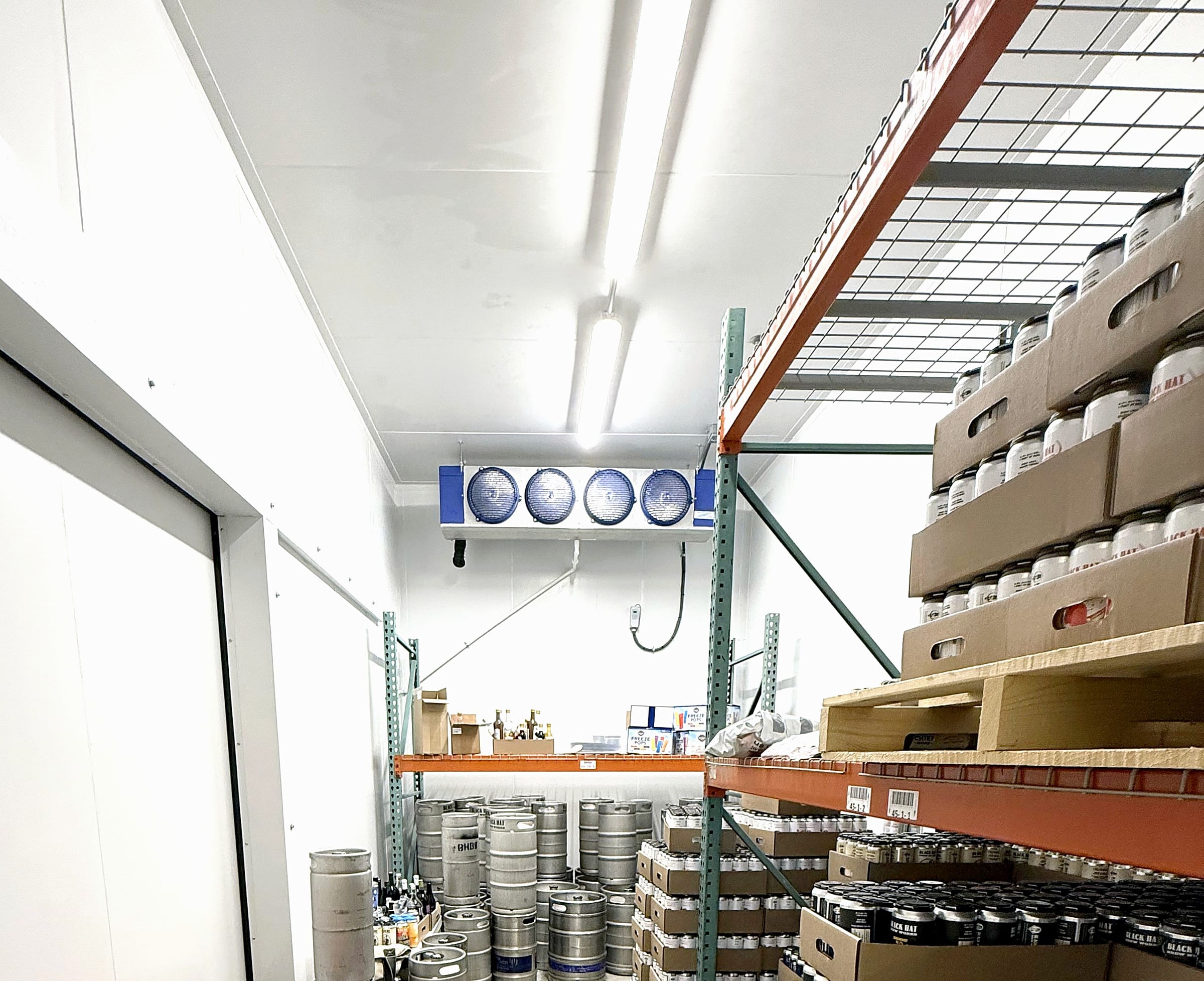 Stocked walk-in cooler at Black Hat Brew Works: kegs on the floor, cases on the racking, cans to the ceiling