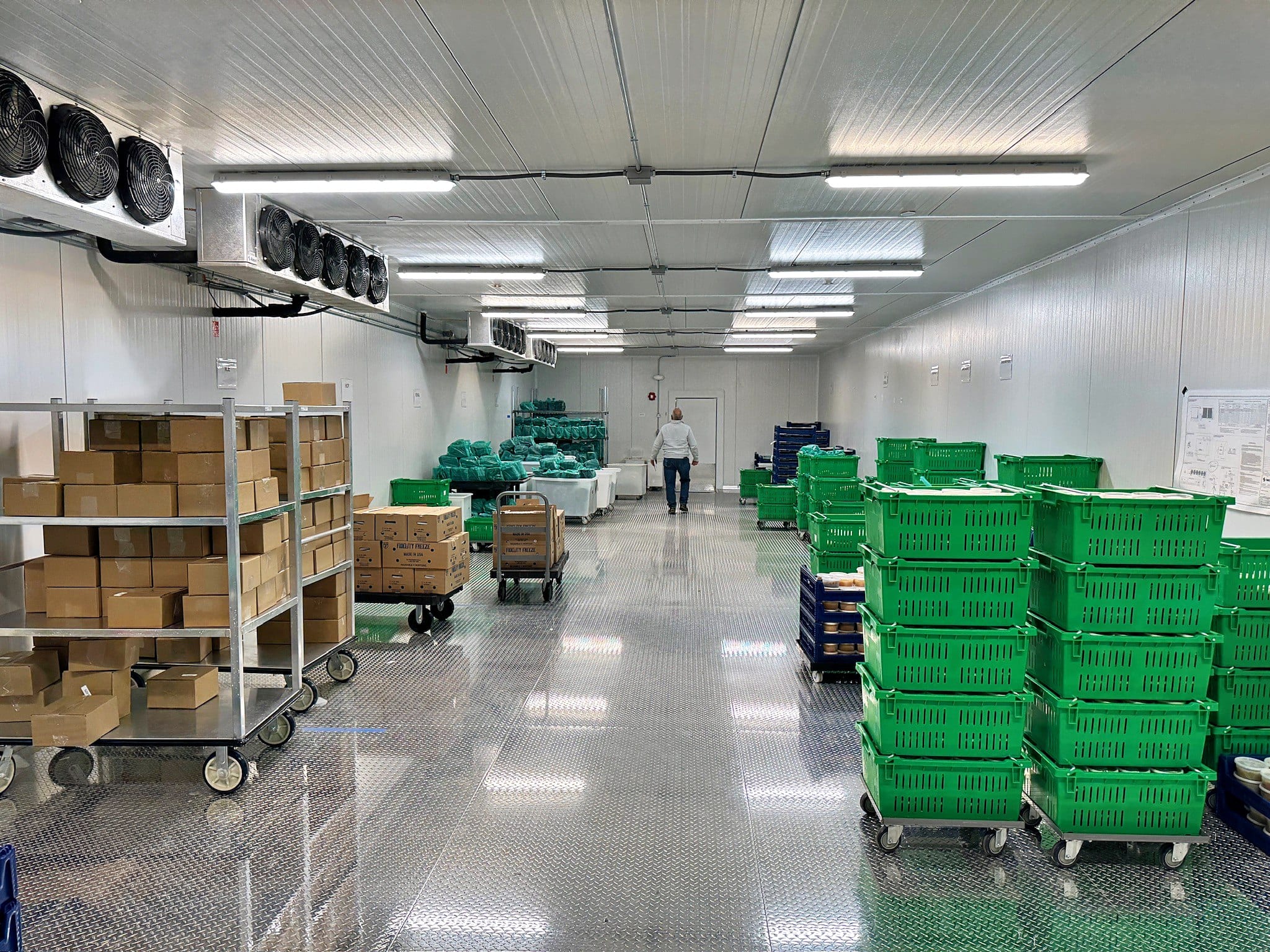 Staff moving green produce totes and cartons of food down the aisle of the Community Servings cooler in Mansfield, MA