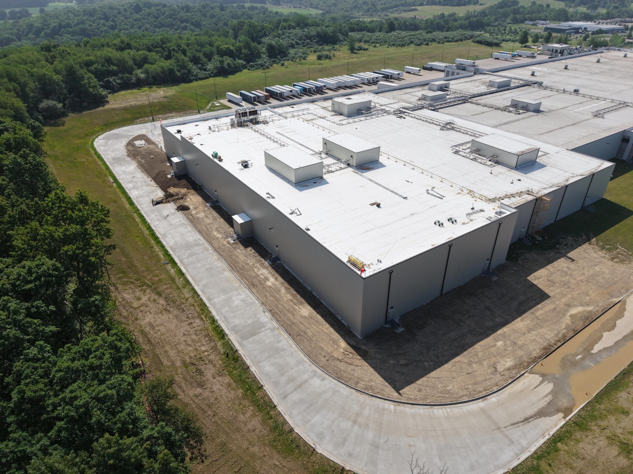 Drone view of a finished insulated metal panel cold storage building addition with a white roof beside a loading dock