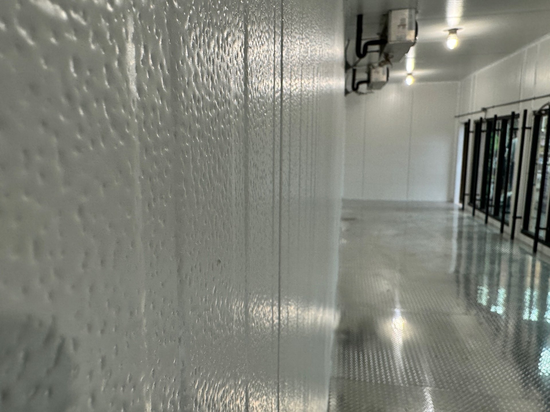 Textured white panel wall inside the Yankee Spirits cooler in Sturbridge, MA, with the glass door line beyond it